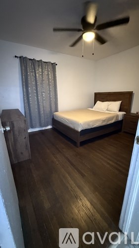 A bedroom with a bed, wooden floor, and a ceiling fan.