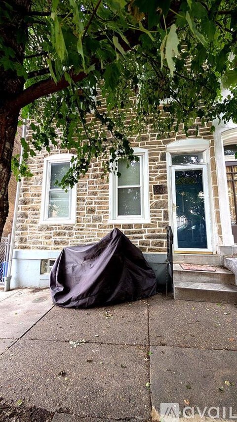 A black tarp is covering a piece of furniture on a sidewalk.