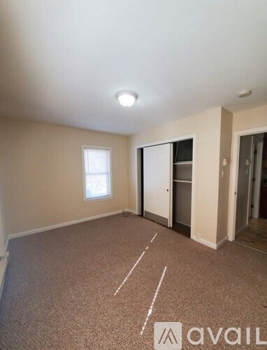A carpeted room with a window and a door leading to another room.