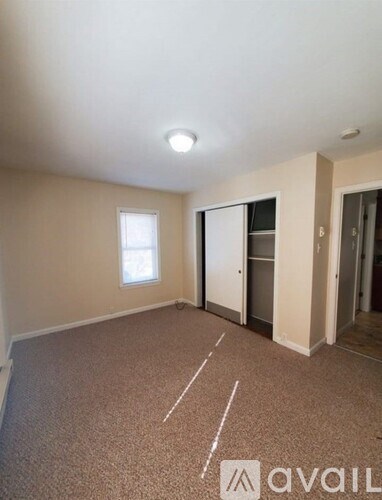 A carpeted room with a window and a door leading to another room.