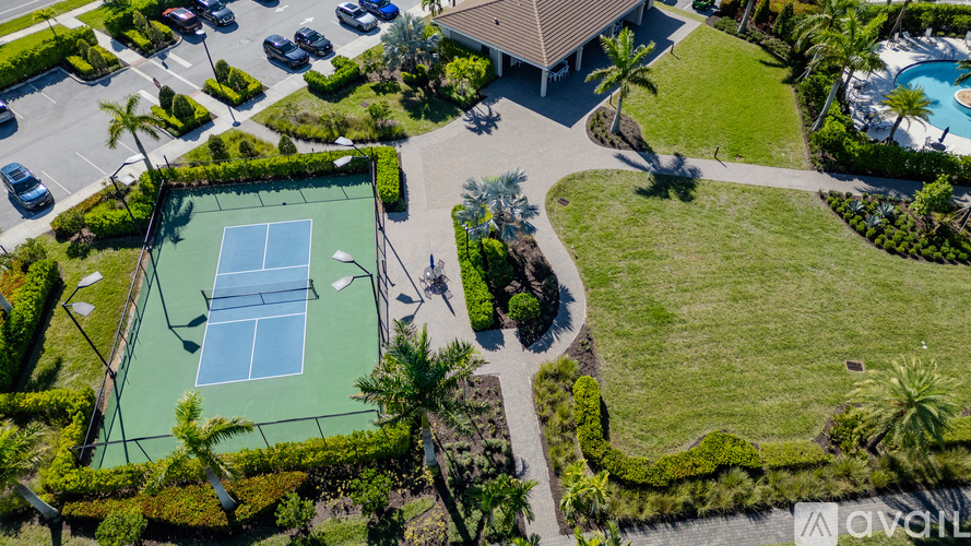 An aerial view of a tennis court surrounded by greenery and a pool.