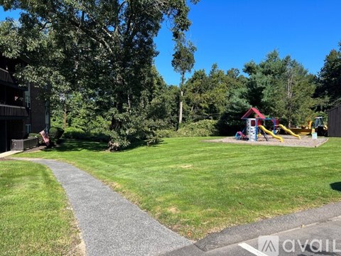 A playground with a slide and swings is surrounded by trees and grass.