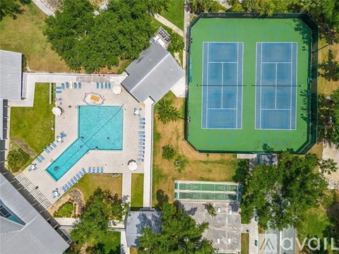 An aerial view of a tennis court and a swimming pool surrounded by trees.