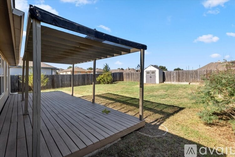A wooden deck with a black awning is in the foreground of a sunny backyard.