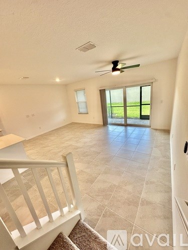 A spacious room with a ceiling fan and a large window overlooking a green field.