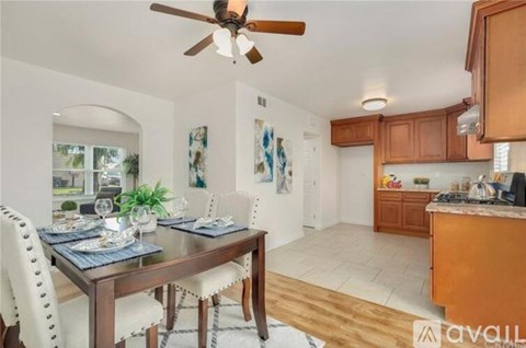 A dining room with a table set for two and a kitchen area with brown cabinets.