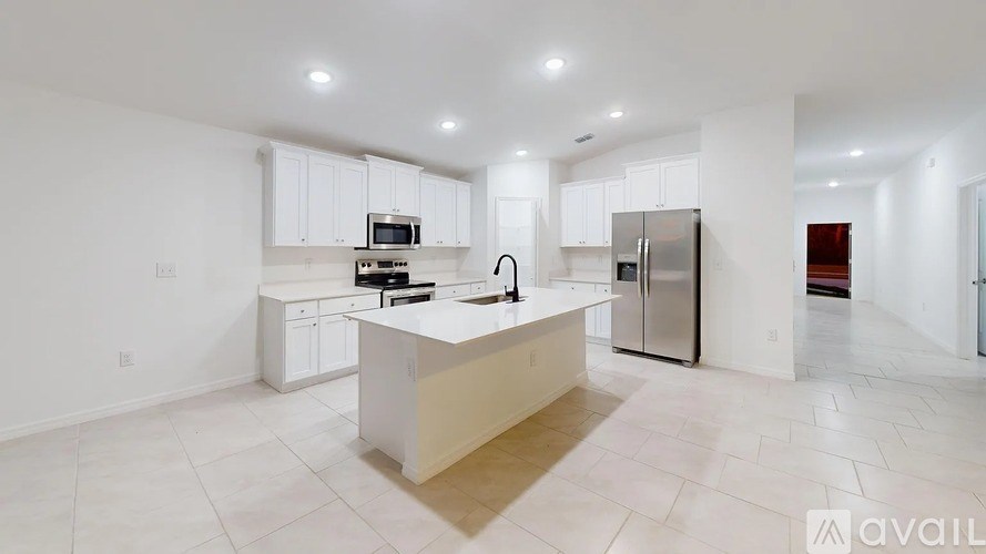 A kitchen with white cabinets and appliances, a central island, and a tiled floor.