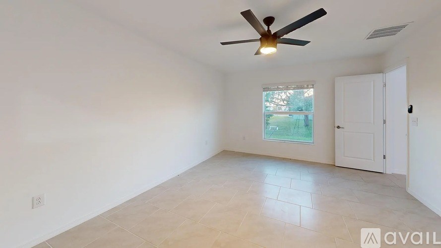 A room with a ceiling fan and a window showing a view of a backyard.