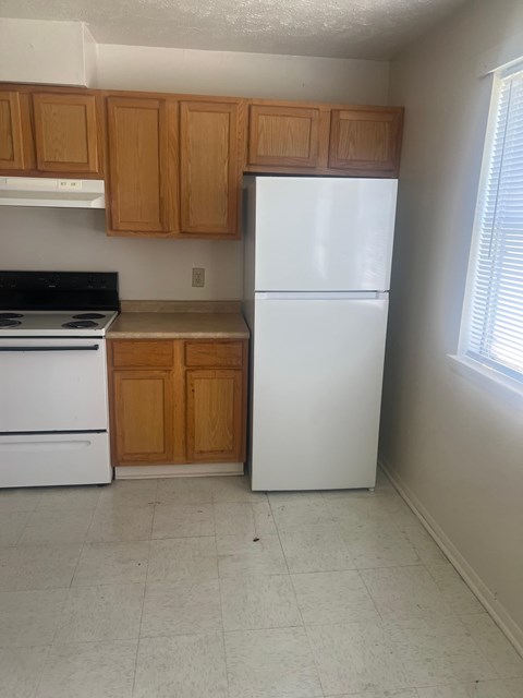 A white refrigerator sits in a kitchen with wooden cabinets.