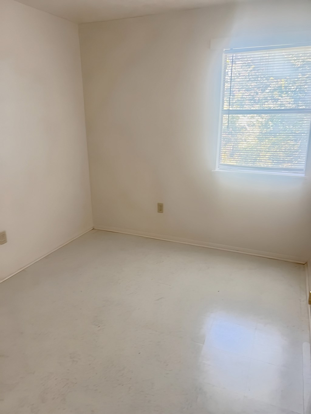 A white room with a window and a light switch on the wall.