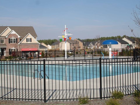 A pool surrounded by a black fence with a house and a flag in the background.