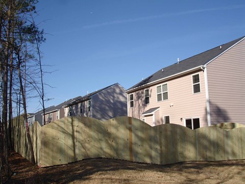 A wooden fence separates a grassy area from a row of houses.