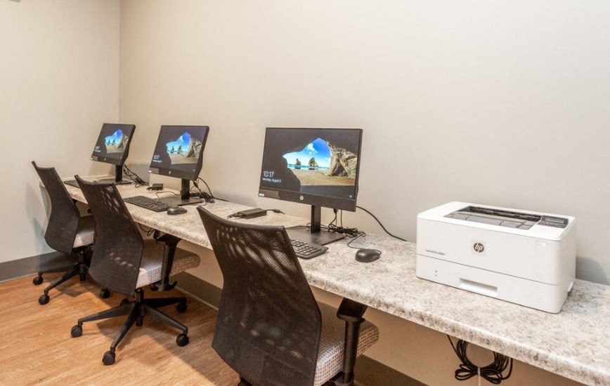 A room with a desk, chairs, and three monitors.