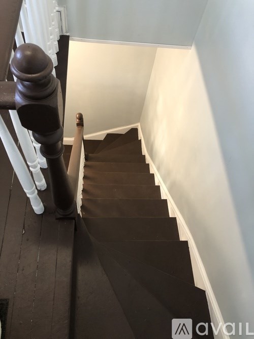 A staircase with a dark carpeted runner and white balusters.