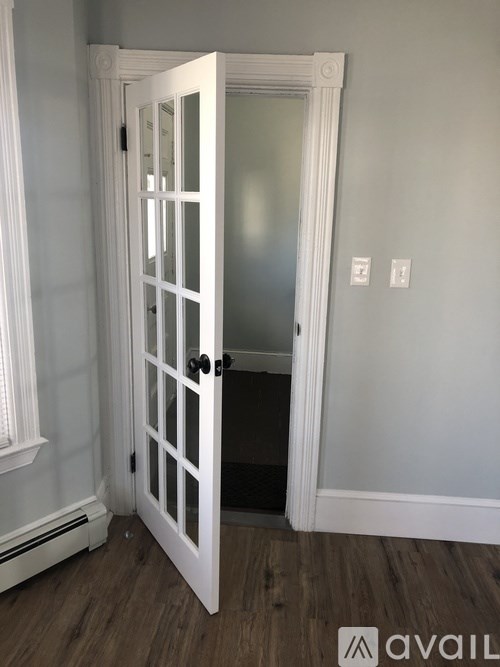 A white door with a black handle is open to a hallway.