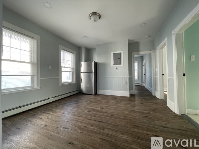 A spacious room with wooden floors and a refrigerator in the corner.