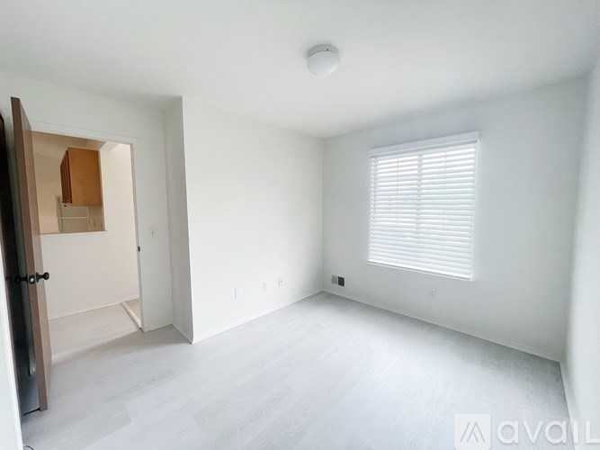 A spacious, empty room with a door on the left and a window with blinds on the right.