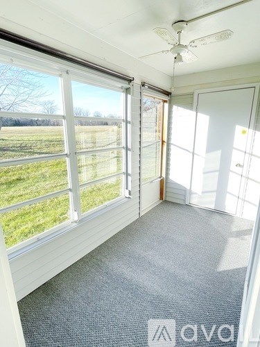 A room with a carpet floor, a ceiling fan, and a view of a field through the windows.