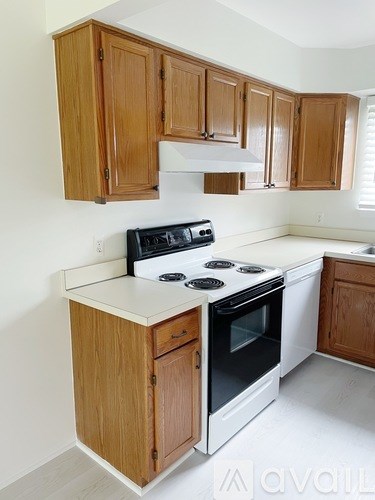 A kitchen with a white stove top oven and wooden cabinets.
