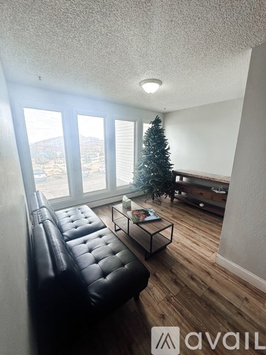 A living room with a black leather couch and a small Christmas tree.