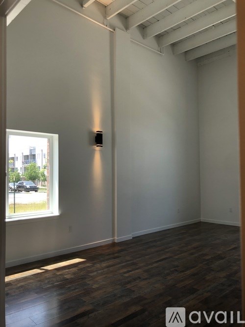 A room with wooden floors and a window showing a parking lot outside.