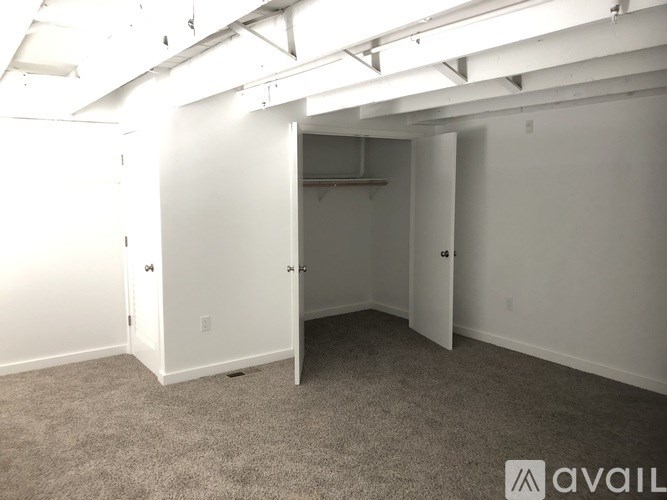 A room with white walls and carpeted floor with a doorway leading to another room.