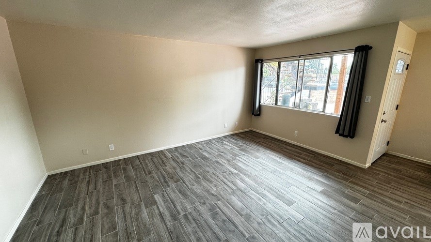 A room with wooden flooring and a window with black curtains.