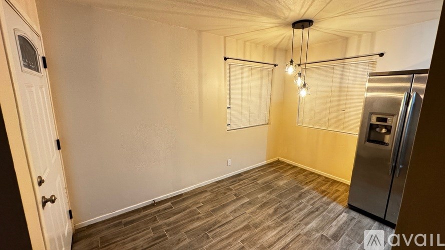 A kitchen with a refrigerator, wooden flooring, and a ceiling light fixture.