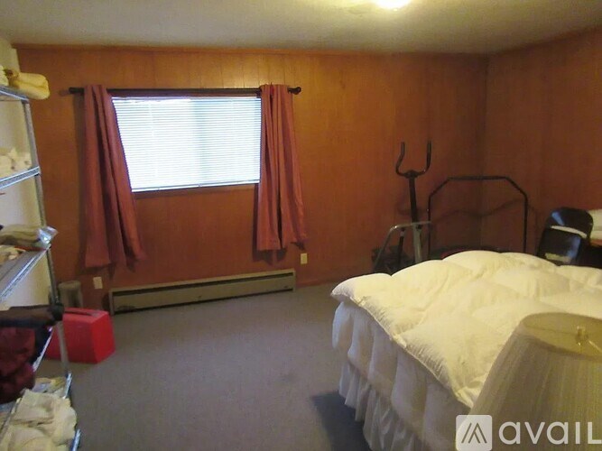 A bedroom with a white bed and a window with red curtains.