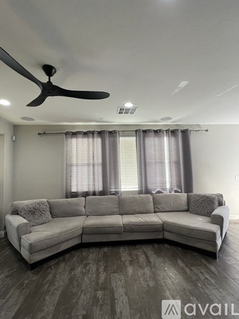 A modern living room with a grey sofa and a ceiling fan.