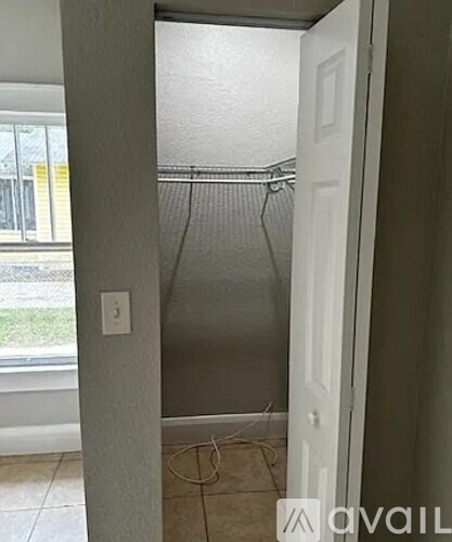 A room with a white door and a window with a view of a fence and grass.