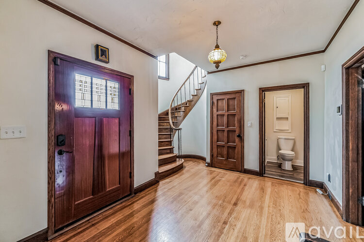 A wooden door with a window above it is in a room with a wooden floor and a staircase.