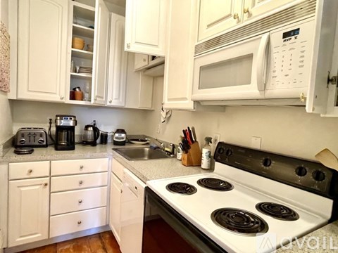 A white kitchen with a stove top oven and a microwave above it.