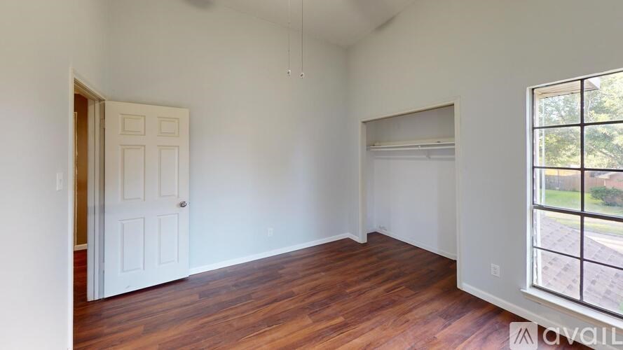 A room with wooden floors and white walls, with a door on the left and a window on the right.