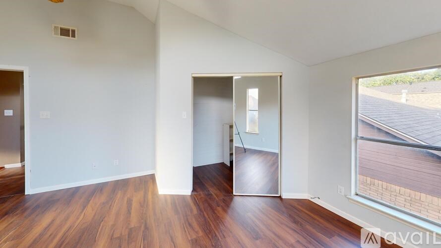 A room with wooden floors and white walls, with a window showing a view of a wooden fence.