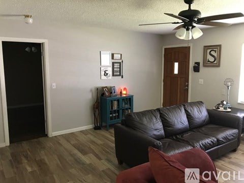 A living room with a black leather couch and a ceiling fan.