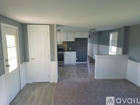 A room with a kitchen area in the background and a white door.