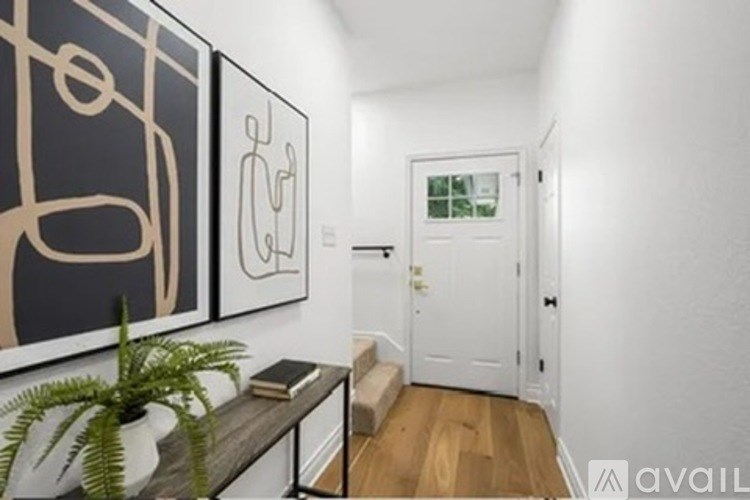 A hallway with a plant on a table and two paintings on the wall.