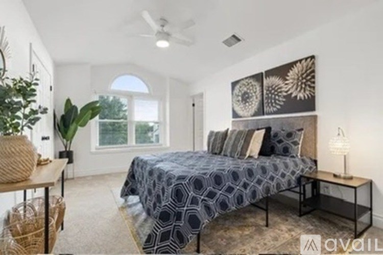 A bedroom with a bed, a table with a lamp, and a plant.