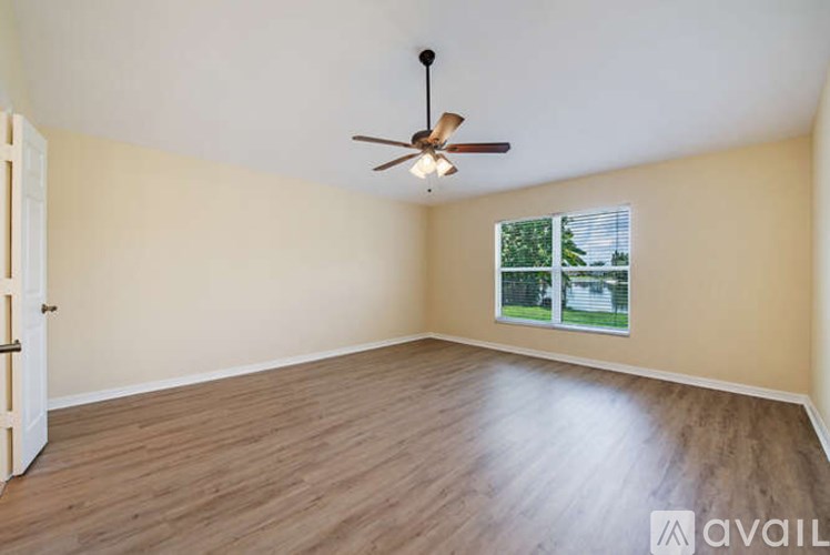 A room with a ceiling fan and a window showing a view of trees and a house.