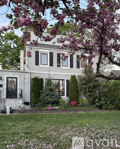 A house with a balcony and a tree with pink flowers in front.
