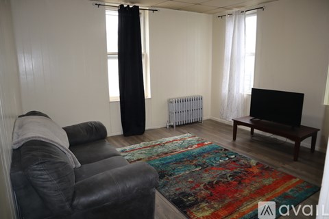 A person is sitting on a black leather couch in a living room with a rug, a television, and a radiator.