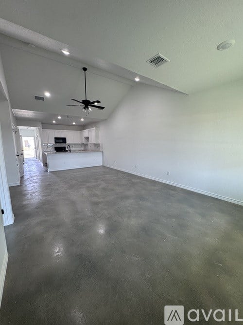 A spacious room with a ceiling fan and a kitchen area in the background.