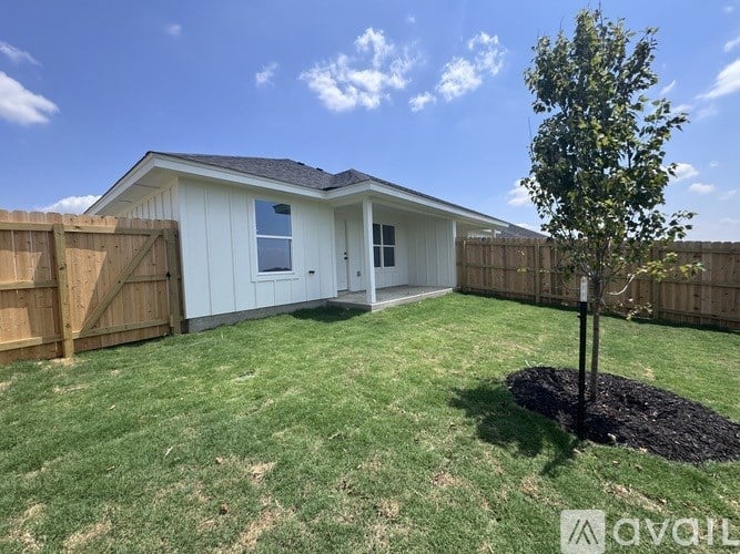 A small white house with a brown fence and a tree in the front yard.
