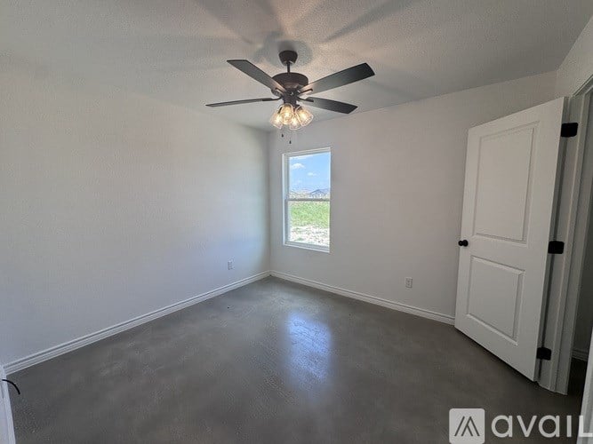 A room with a ceiling fan and a window showing a view of a grassy area.