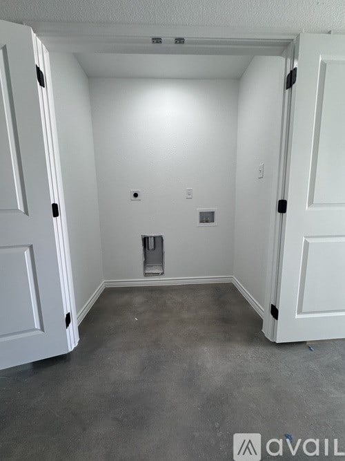 A room with white walls and a grey floor with a white door on the left and a white cabinet on the right.