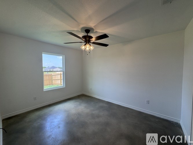 A room with a ceiling fan and a window overlooking a fence.