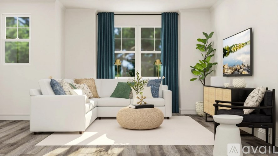 A modern living room with a white sofa, a round wicker ottoman, and a large window with blue curtains.