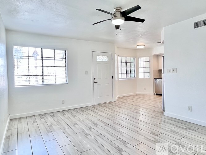 A room with a ceiling fan and light, hardwood floors, and a window with blinds.