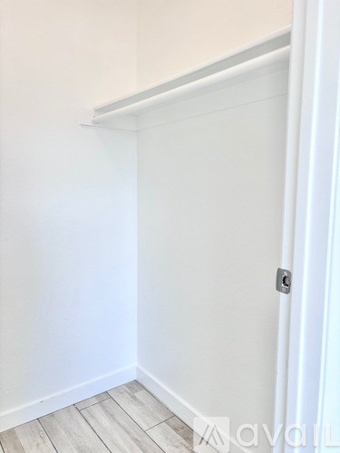 A white door with a silver handle is on the right side of a room with white walls and wooden flooring.